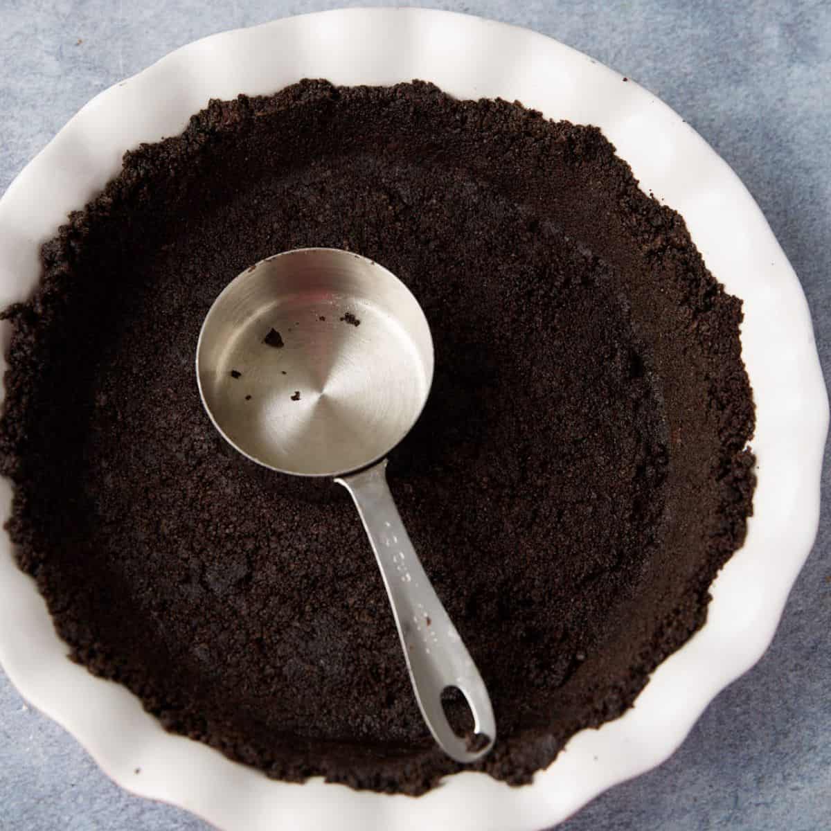 An oreo cookie crust in a pie pan with a measuring cup.