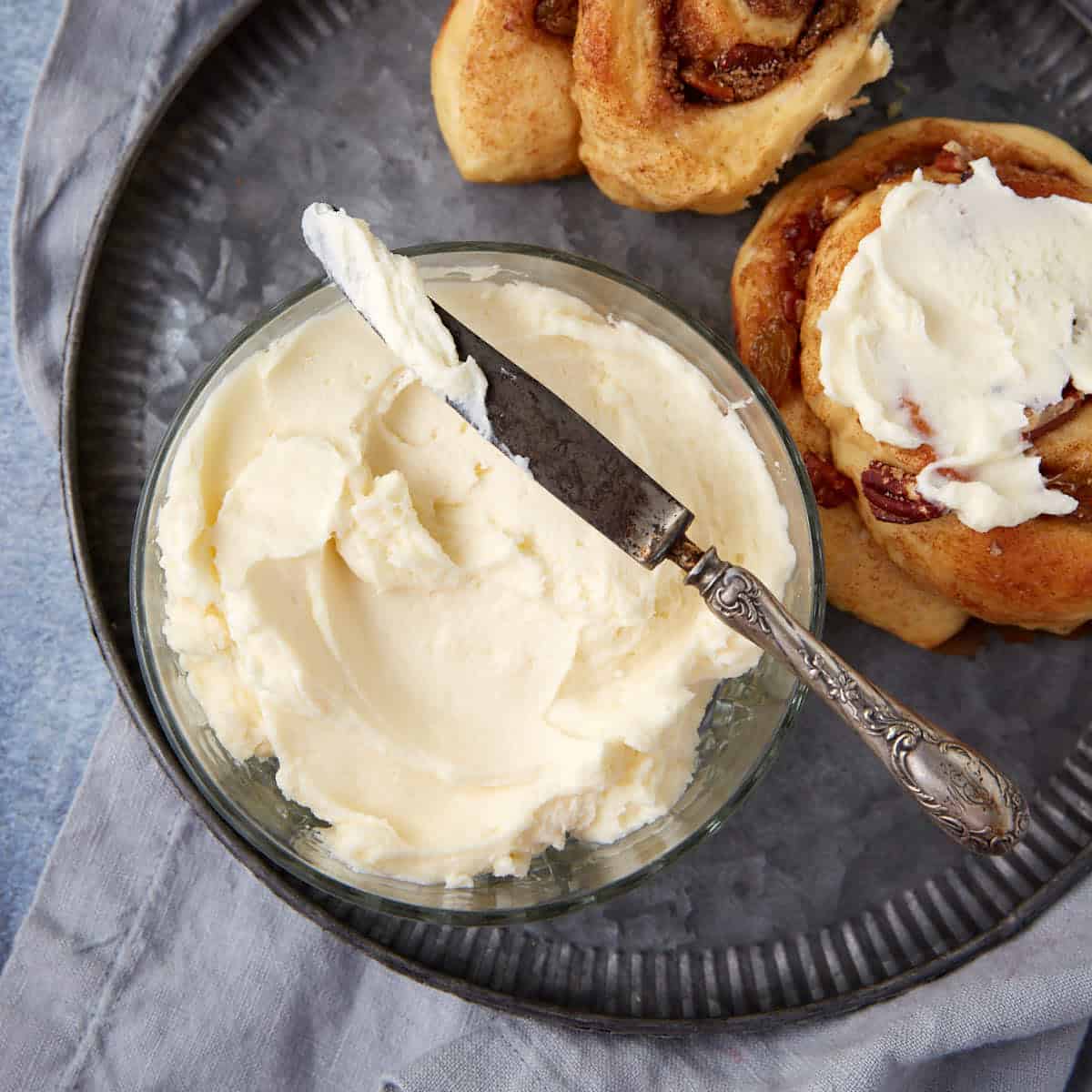 Cream cheese frosting in a bowl next to a frosted cinnamon roll.