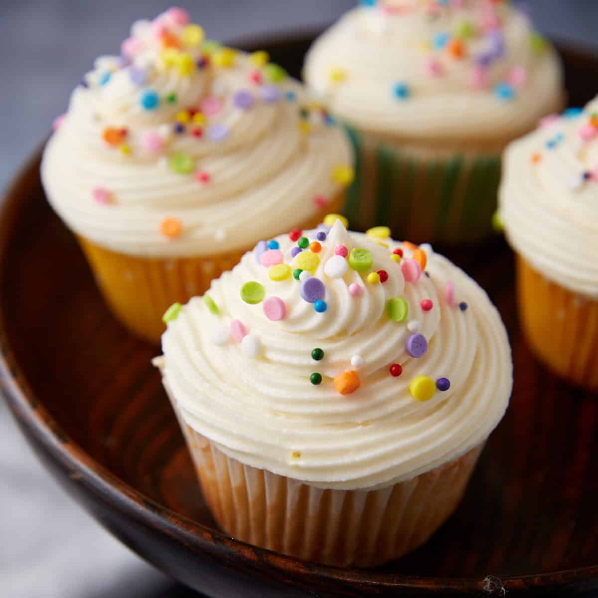 Multi colored sprinkles on frosted lemon cupcakes.