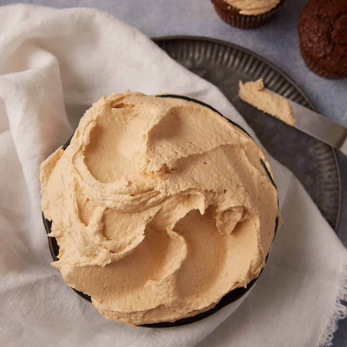 A bowl of peanut butter cream cheese frosting next to a frosted cupcake.