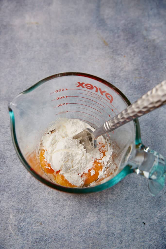 half and half, sugar, salt, cornstarch, and egg yolks in a glass measuring cup with a spoon