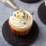 One vanilla cupcake with vanilla frosting and sprinkles.