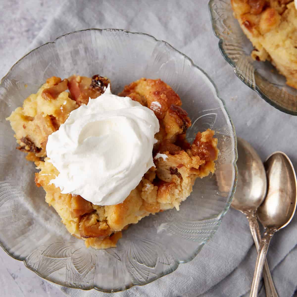 close up of apple bread pudding on a glass plate with whipped cream on top.