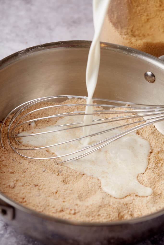 milk being added to the brown sugar custard mixture in a saucepan.