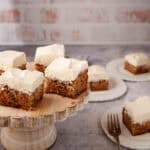 squares of carrot cake sheet cake with cream cheese frosting on a cake platter.
