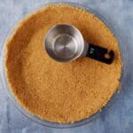 A measuring cup inside a graham cracker pie crust.