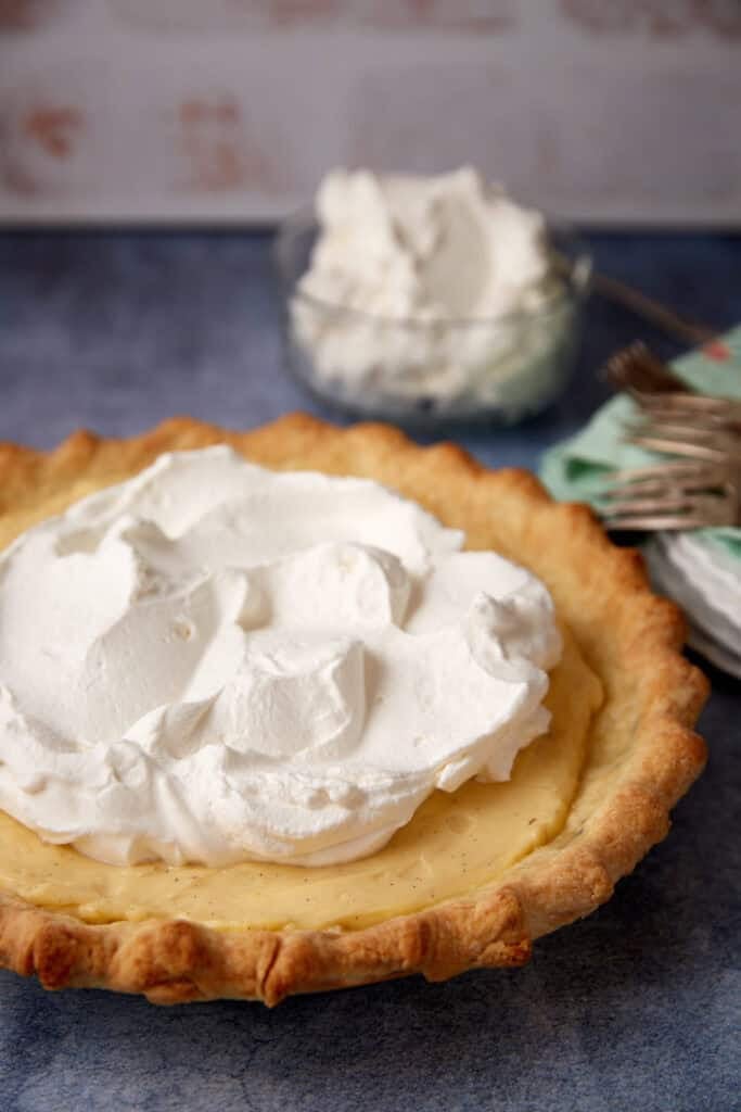 vanilla pudding pie on a gray background with extra whipped cream behind it.