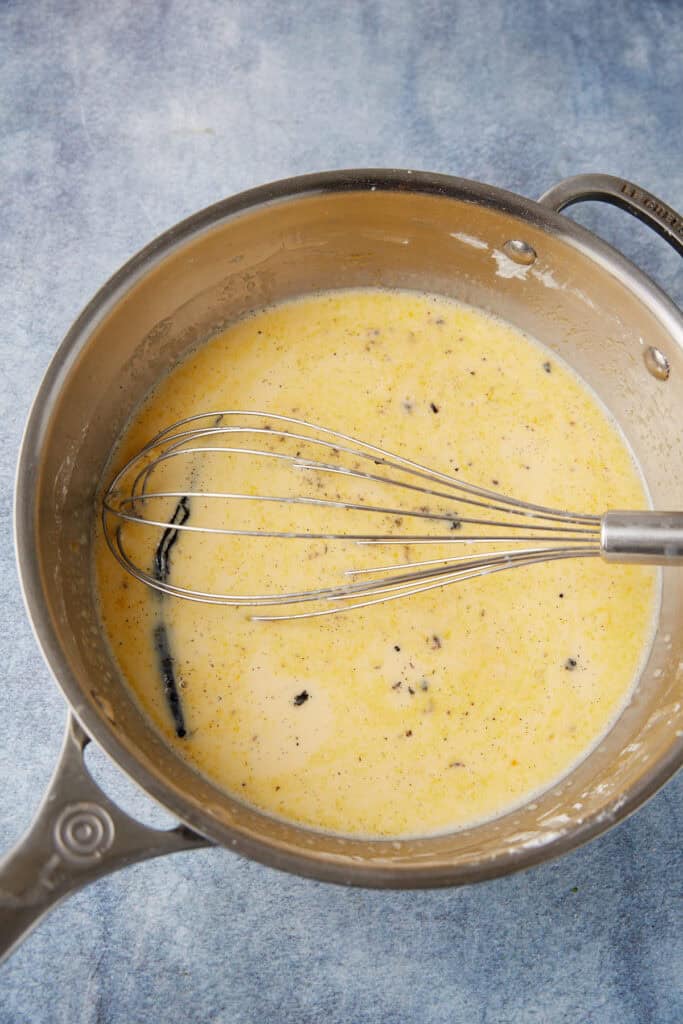 custard mixture in a saucepan with a vanilla bean in it.