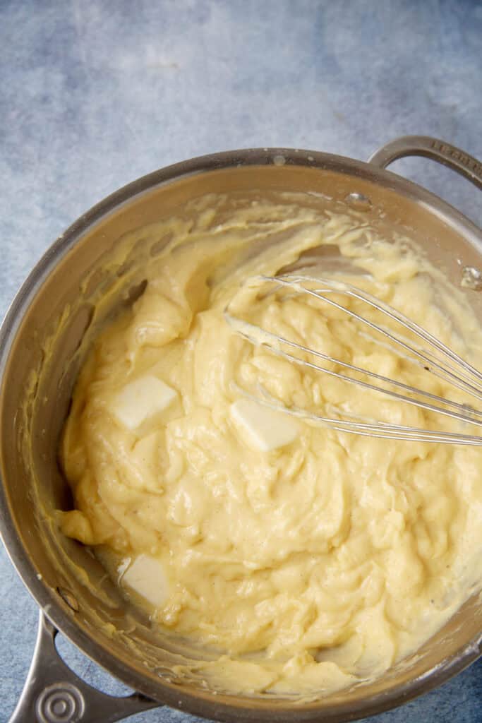 pats of butter being whisked into the custard mixture in a saucepan.