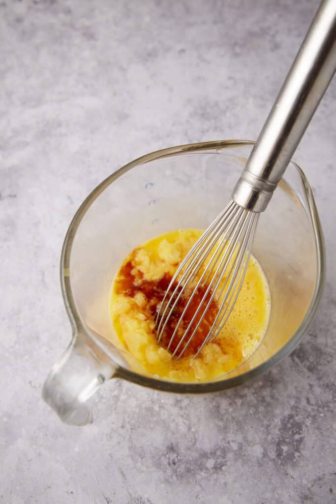 eggs, vanilla, and crushed pineapple in a glass measuring cup with whisk. 