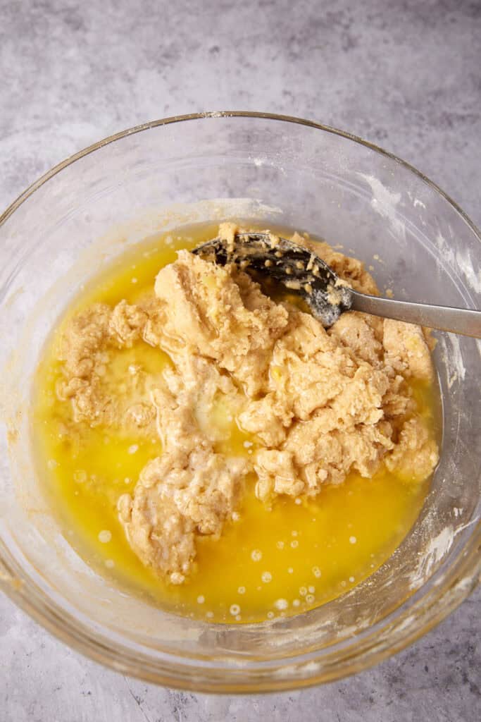 melted butter being mixed into batter in a glass bowl.