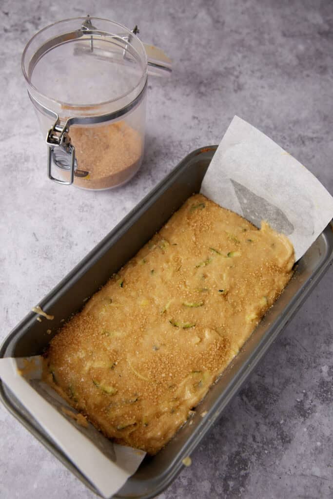 pineapple zucchini bread batter in loaf pan lined with parchment paper and sprinkled with sugar.