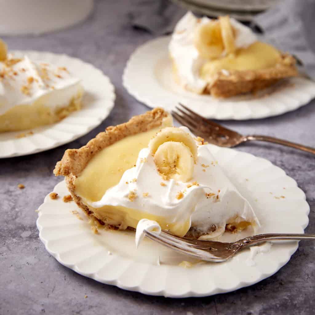 slices of banana cream pie on white plates with forks.