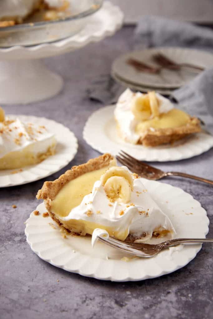 slices of banana cream pie on white plates with forks.
