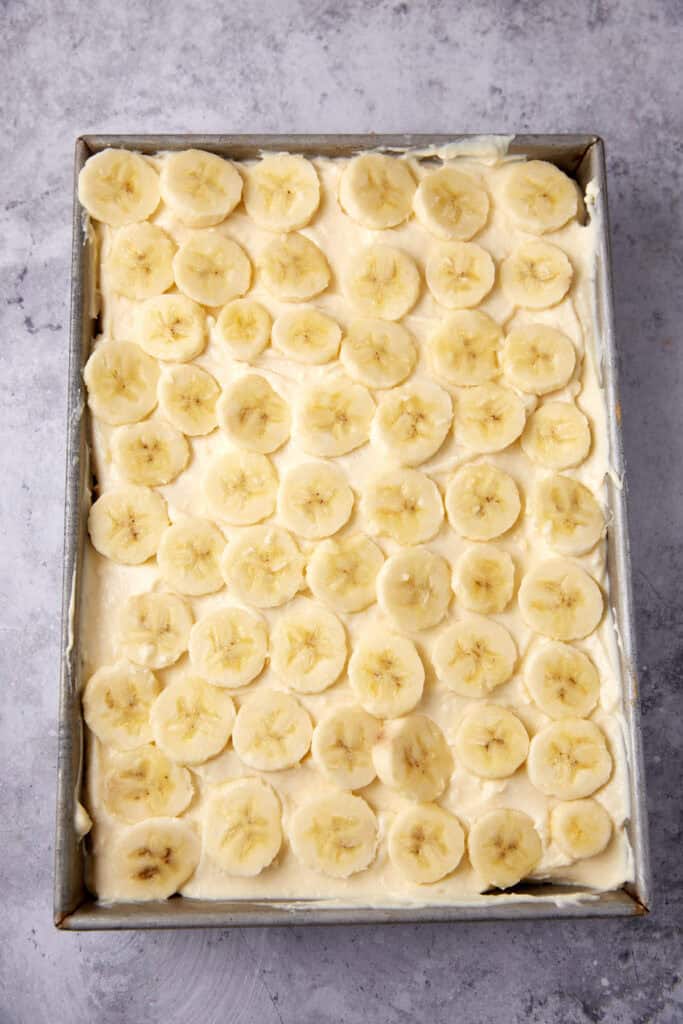 banana pudding poke cake with a layer of sliced bananas on to.