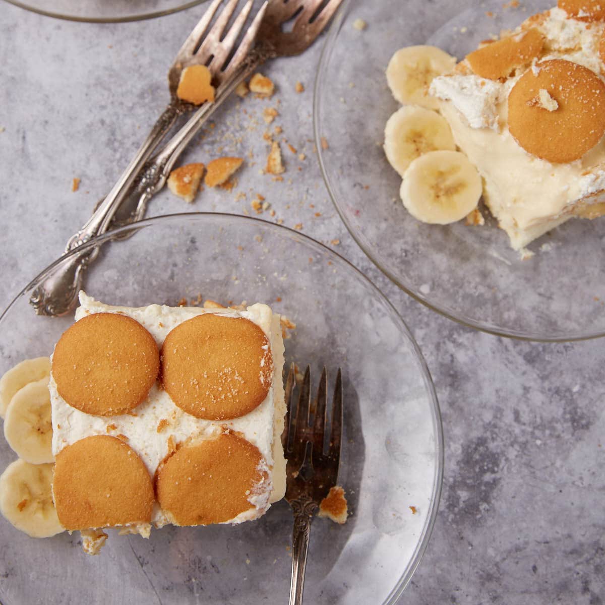 2 slices of banana pudding poke cake on glass plates with forks on the side.