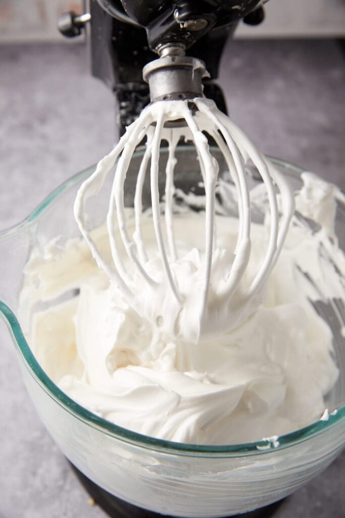 A mixer blending whipped cream in a stainless steel bowl, with cream swirling around the beaters.