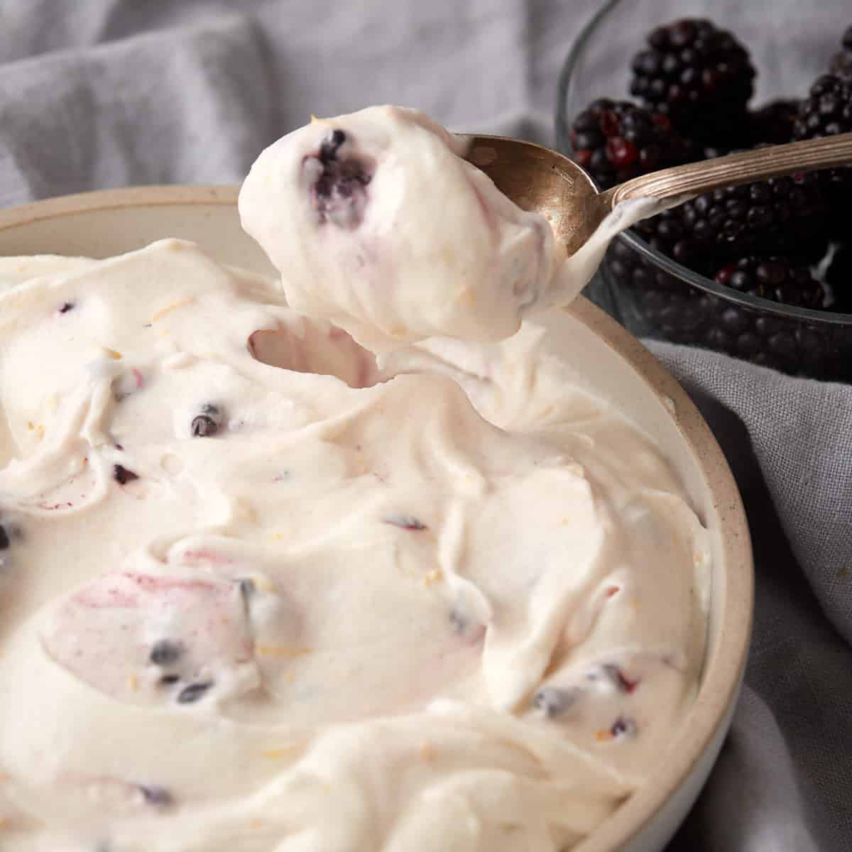 blackberry cream cheese frosting in a bowl with a spoon lifting up out of the bowl.