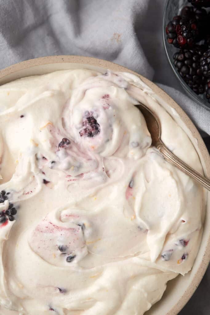 blackberry cream cheese frosting in a bowl with a spoon lifting up out of the bowl.