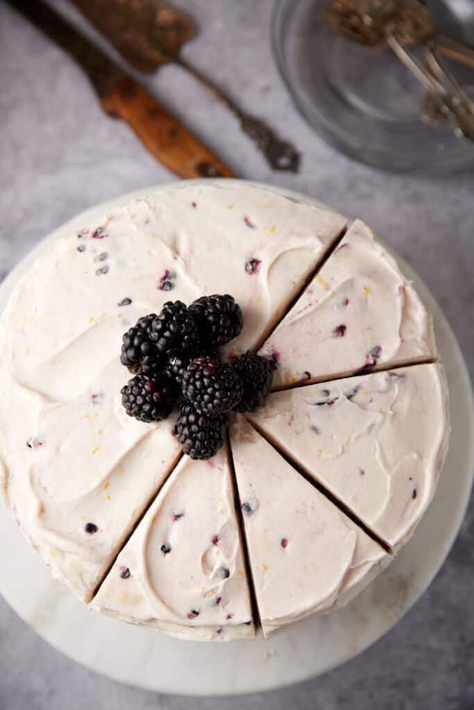 blackberry jam cake fully frosted on a white cake stand topped with blackberries.