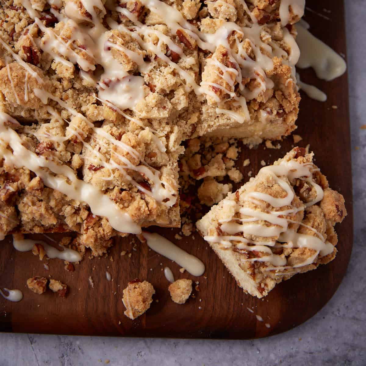 close up of glazed crumb cake on a wooden cutting board.