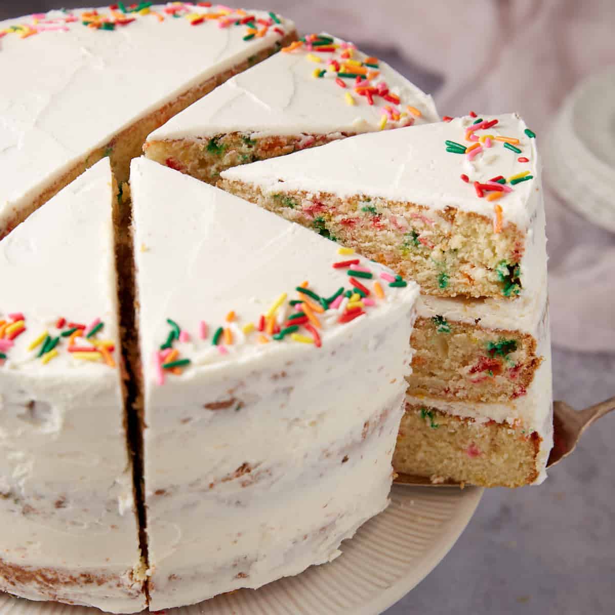 confetti cake on a white cake stand sliced into pieces.