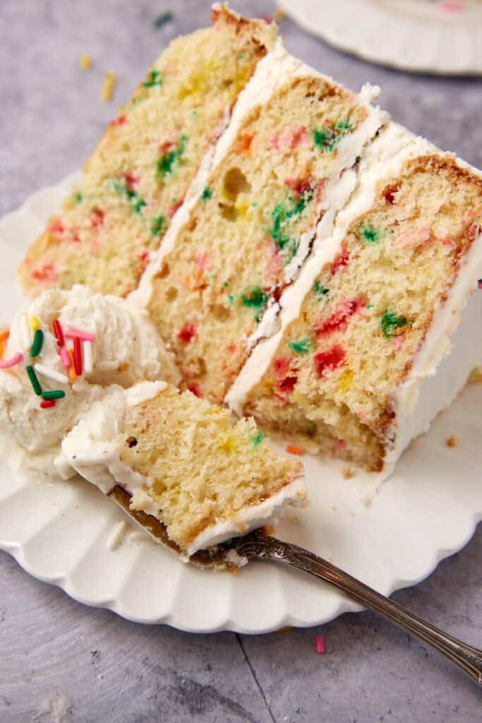 slice of confetti cake on a white plate with a fork and a piece of cake on the fork.