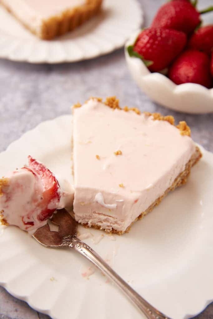 a slice of frozen strawberry pie on a white plate with a bite on a fork laying next to the slice.