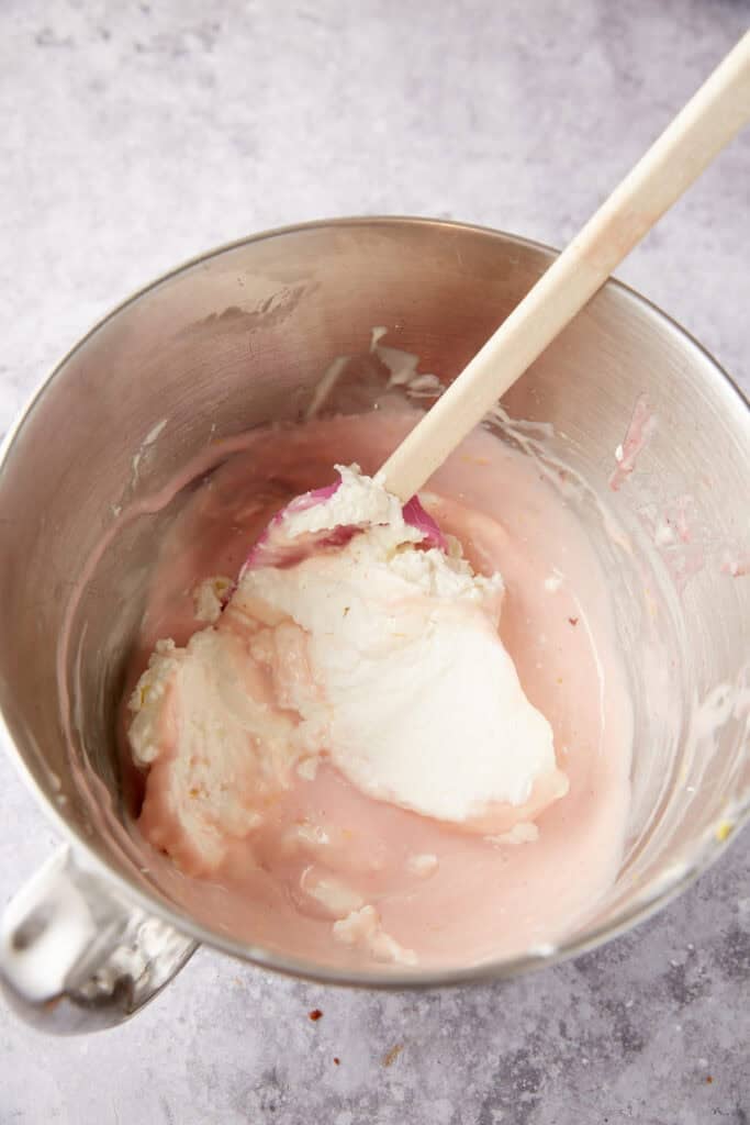 whipped cream being folded into the strawberry condensed milk and cream cheese layer.
