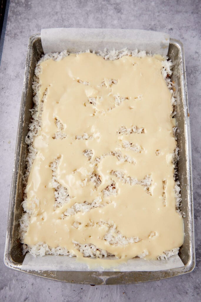 hello dolly bars in a baking pan with condensed milk poured on top.