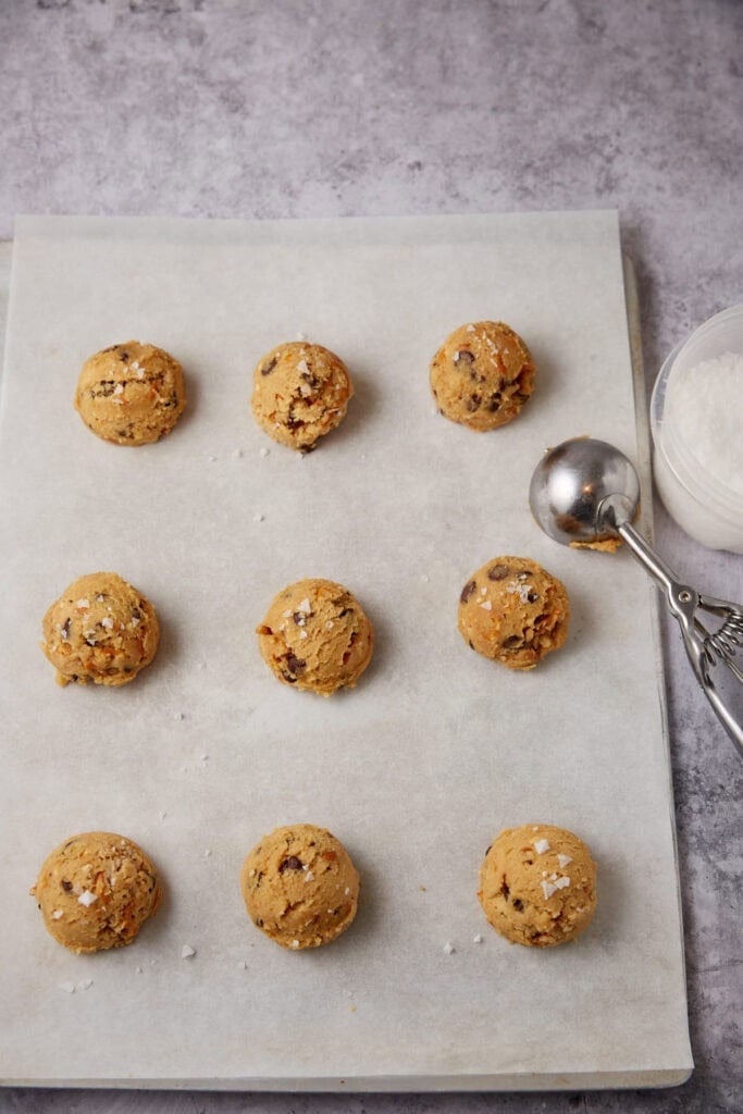 peanut butter pretzel cookie dough balls on a baking sheet with a cookie scoop on the side.