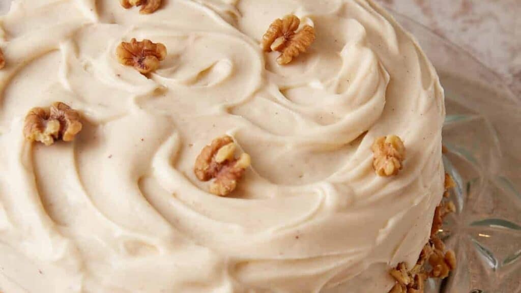 A banana cake with cream cheese frosting with walnuts on top.