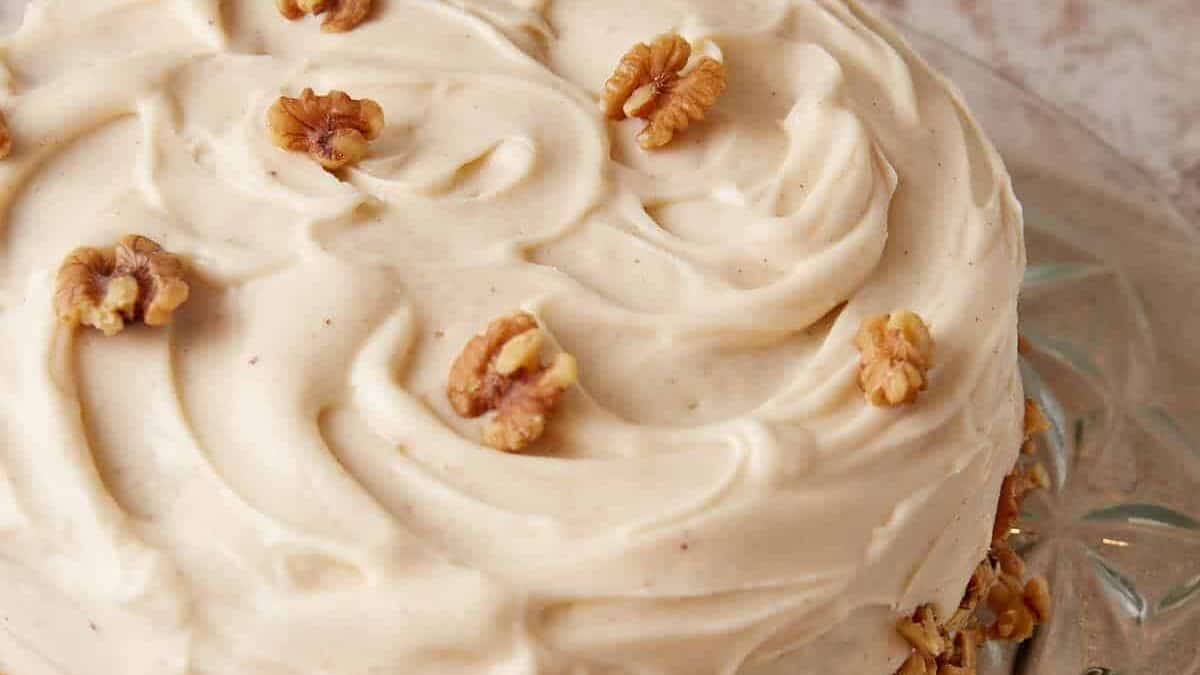 A banana cake with cream cheese frosting with walnuts on top.