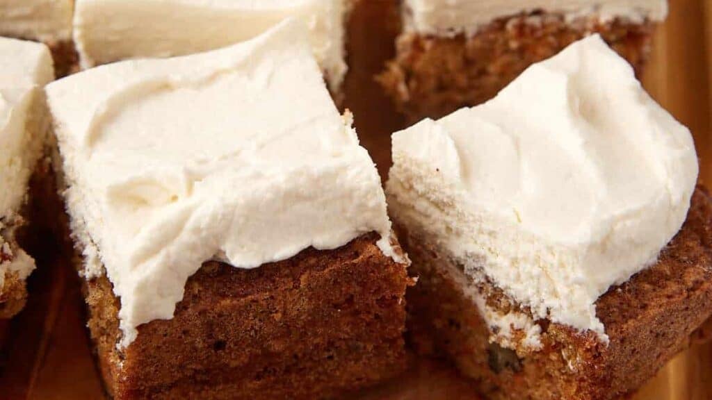 carrot cake sheet cake cut into slices on a wooden cutting board.