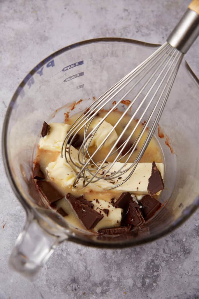 butter and chocolate being melted in a glass measuring cup with a whisk.