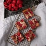 raspberry cream cheese brownies on a wire rack with a bowl of raspberries on the side.