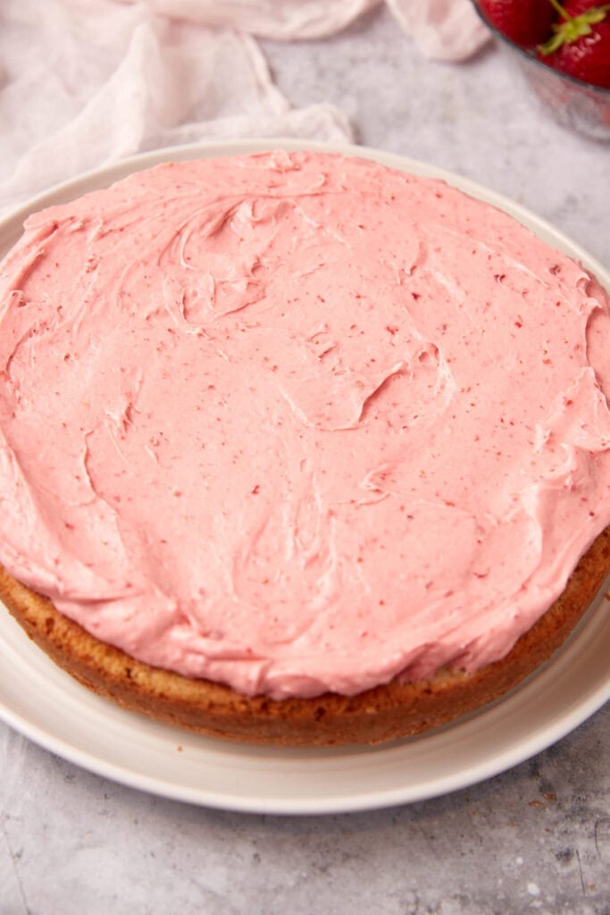 strawberry cake being frosted with strawberry cream cheese frosting.