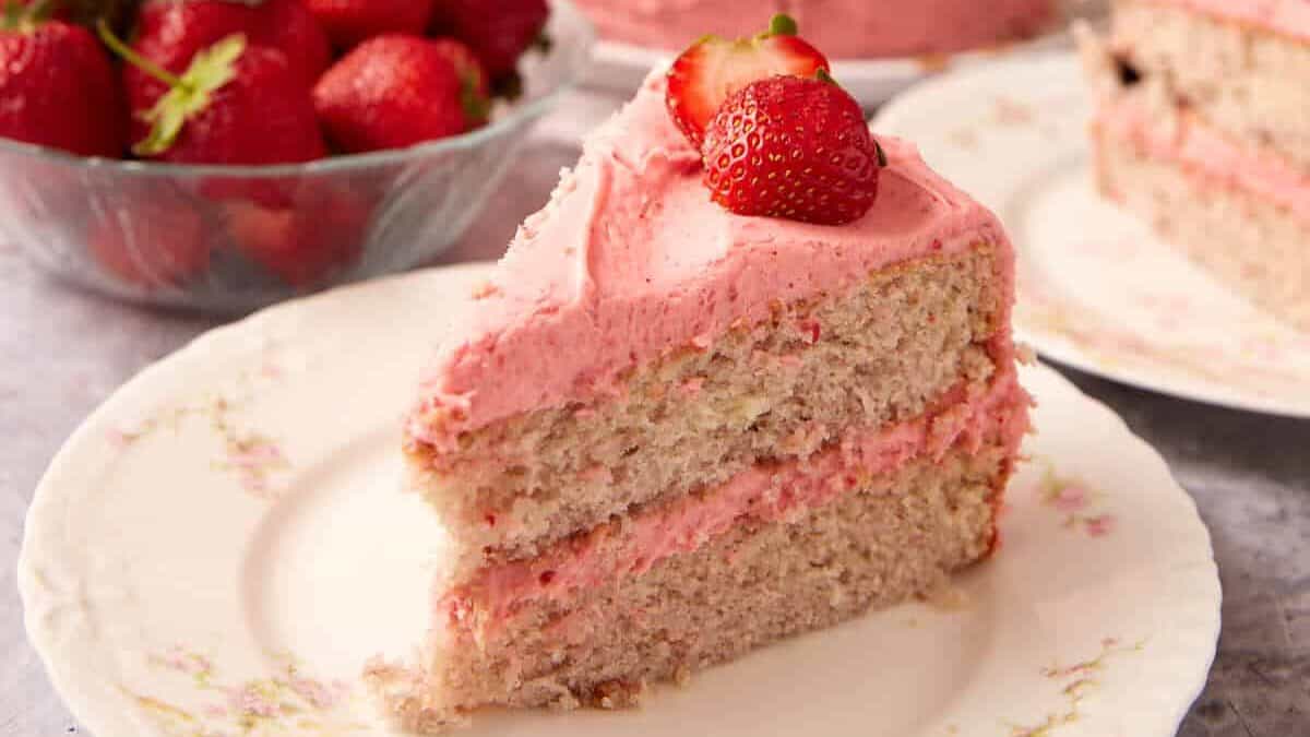 slices of strawberry cake on white plates with the strawberry cake in the background.