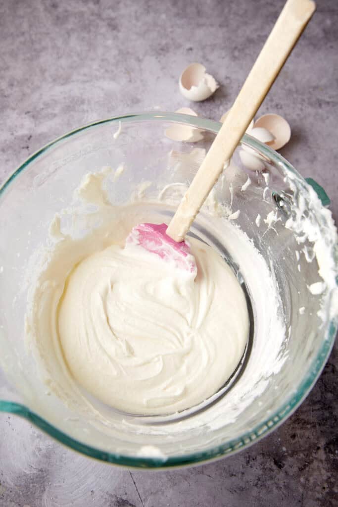 egg whites, sour cream, and vanilla being mixed in a glass bowl with a spatula.