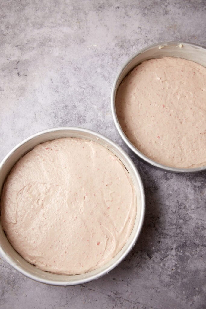 strawberry cake batter poured into cake pans.