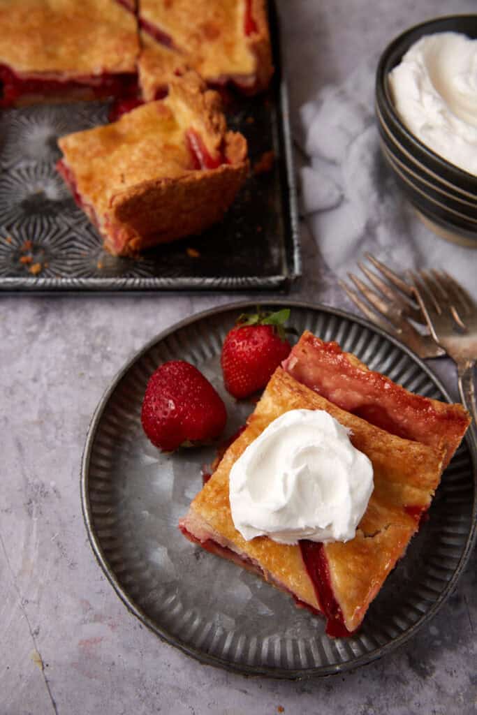 A slice of strawberry pie on a plate with whipped cream.