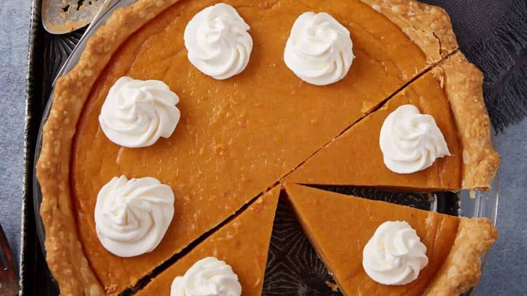 A sweet potato pie next to a bowl of whipped cream.