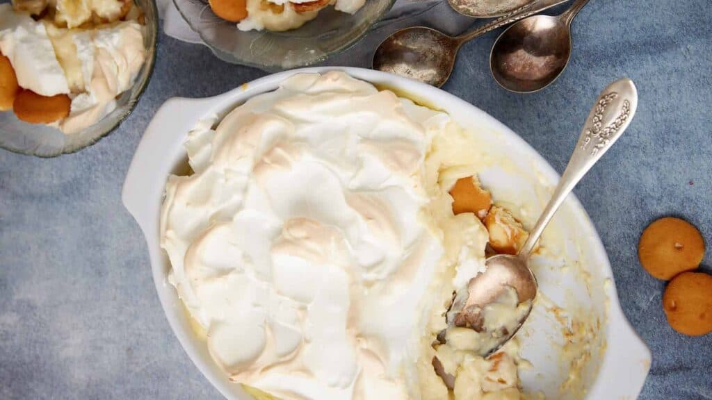 Banana pudding topped with meringue in a baking dish with a serving spoon.