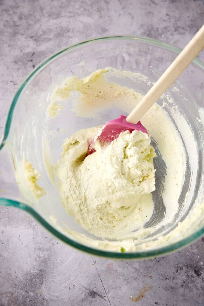 A bowl of creamed butter, sugar, lemon, and lime zest with a wooden spoon.