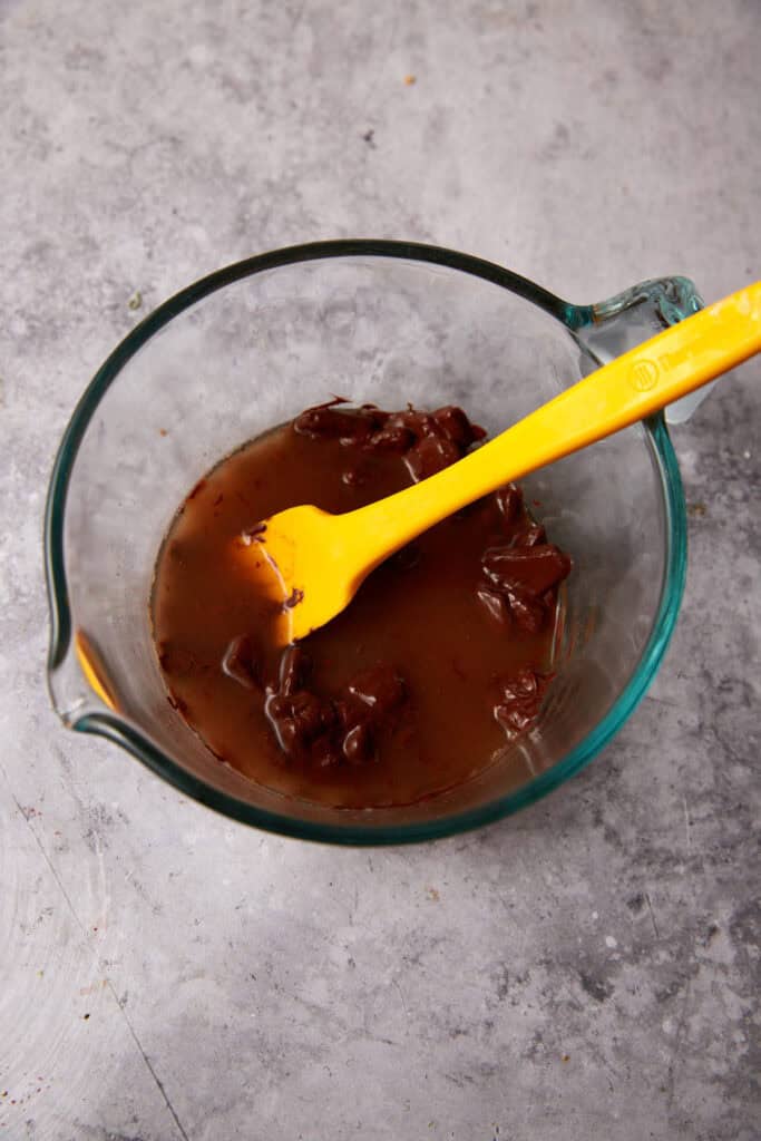 melted chocolate and boiling water in a glass measuring cup with a spatula.