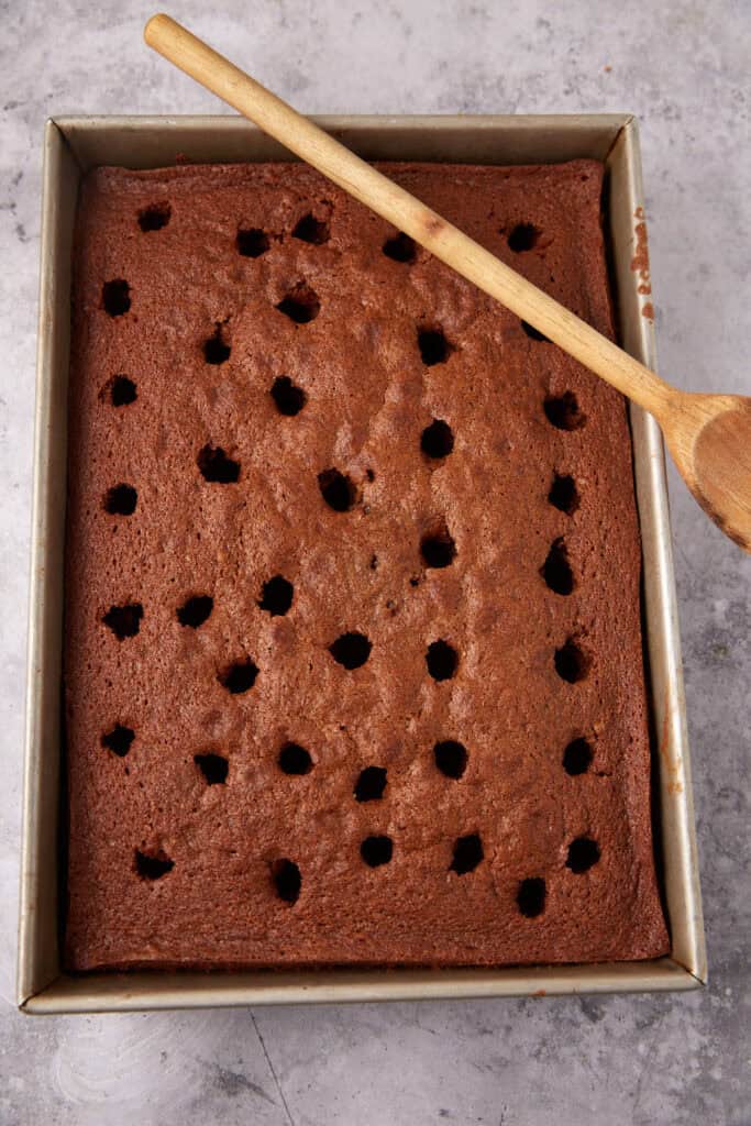 chocolate cake with holes poked into it with a wooden spoon resting on the side.
