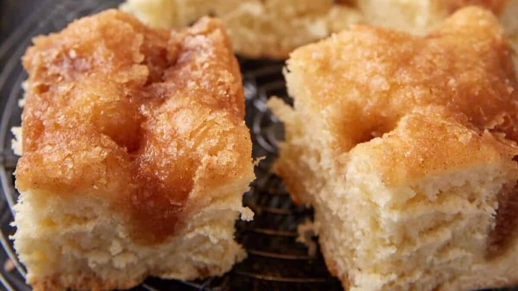Squares of sugar cake next to cups of coffee.