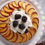 A peach and blackberry cake topped with whipped cream.