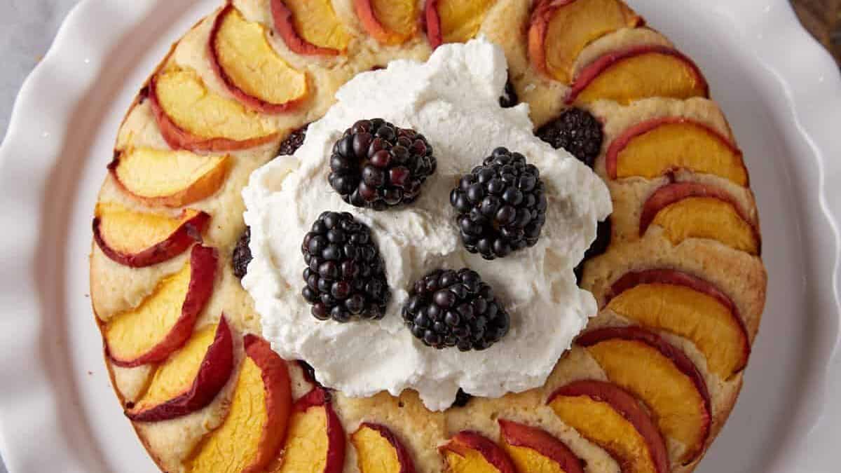 A peach and blackberry cake topped with whipped cream.