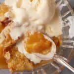 A glass bowl of peach cobbler and ice cream.